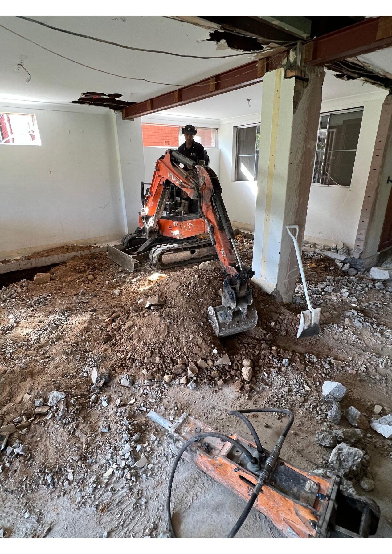 Mini excavator breaking up a slab inside a stripped house at Gymea Bay